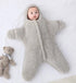 Baby in a fluffy beige snowsuit lying on a white surface with a teddy bear beside.