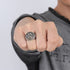 Close-up of a hand wearing a silver ring with a detailed design on a gray background