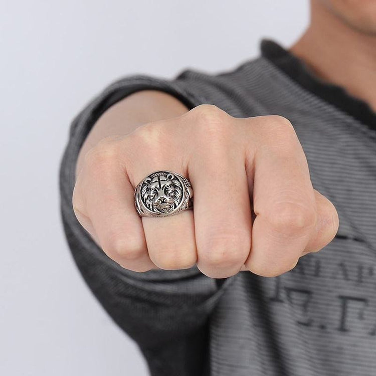 Close-up of a hand wearing a silver ring with a detailed design on a gray background
