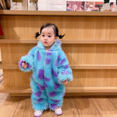 Child wearing a blue and purple fluffy outfit standing in front of wooden shelves.